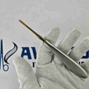 Straight Warwick James dental root elevator with gold titanium working end held in a gloved hand for dental surgery.